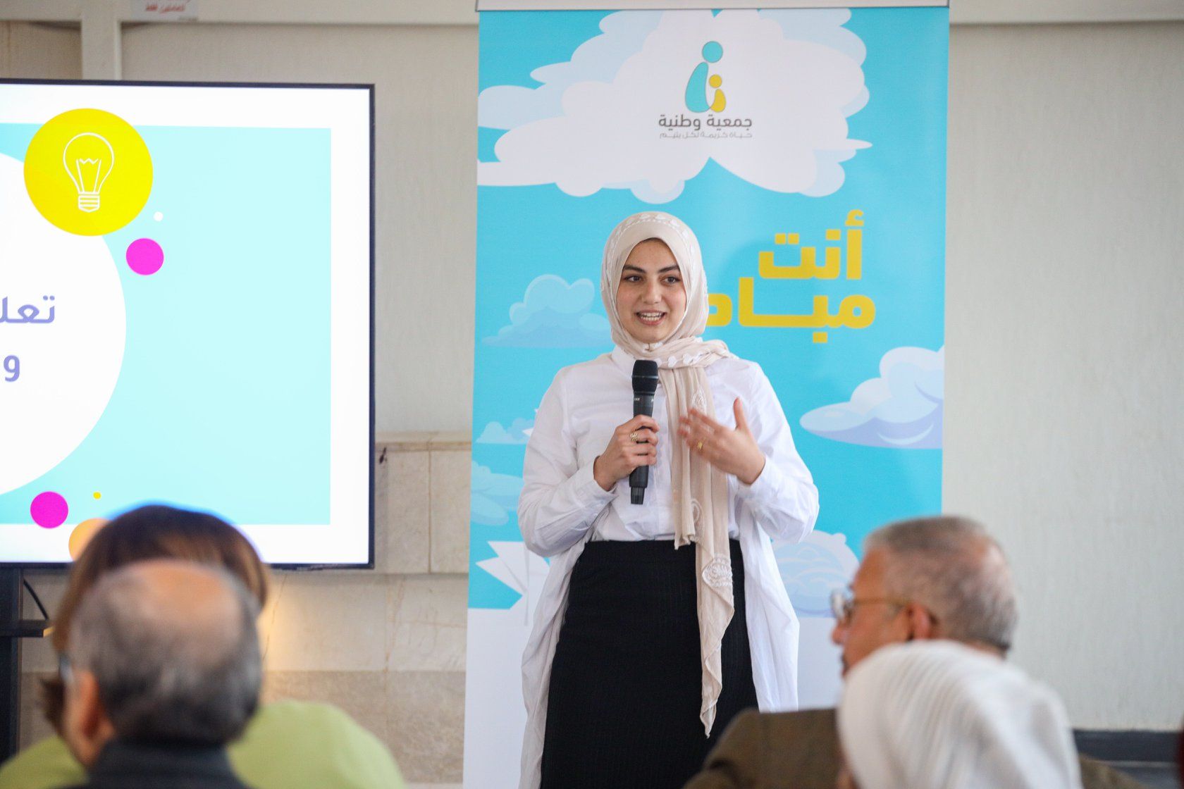 متحدثة أمام جدارية ملونة تخاطب المشاركين